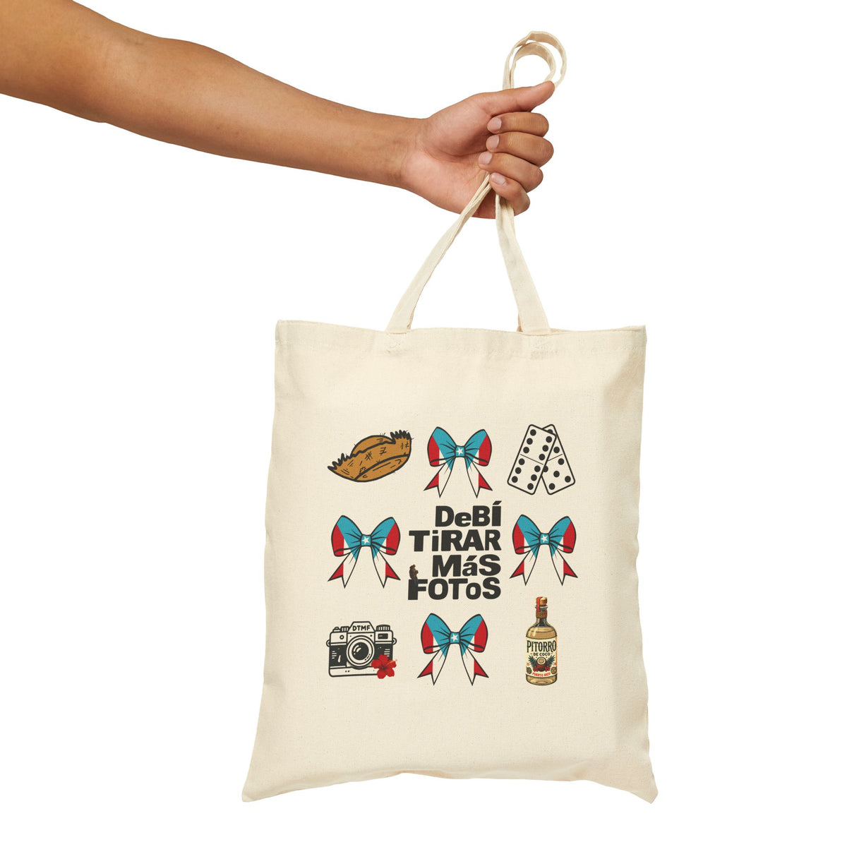 An off-white canvas tote bag with a printed graphic of Mexican-themed icons (hot dog, playing cards, bows, camera, tequila bottle) and the text 'Debi Tirar Más Fotos', held by a person's arm against a white background.