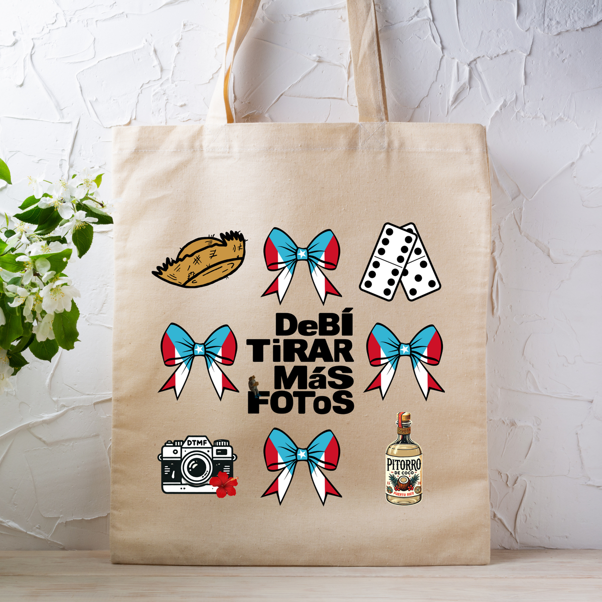 A cream canvas tote bag printed with colorful Puerto Rico-themed illustrations and text, resting on a wooden bench with a black wrought iron railing and green foliage in the background.
