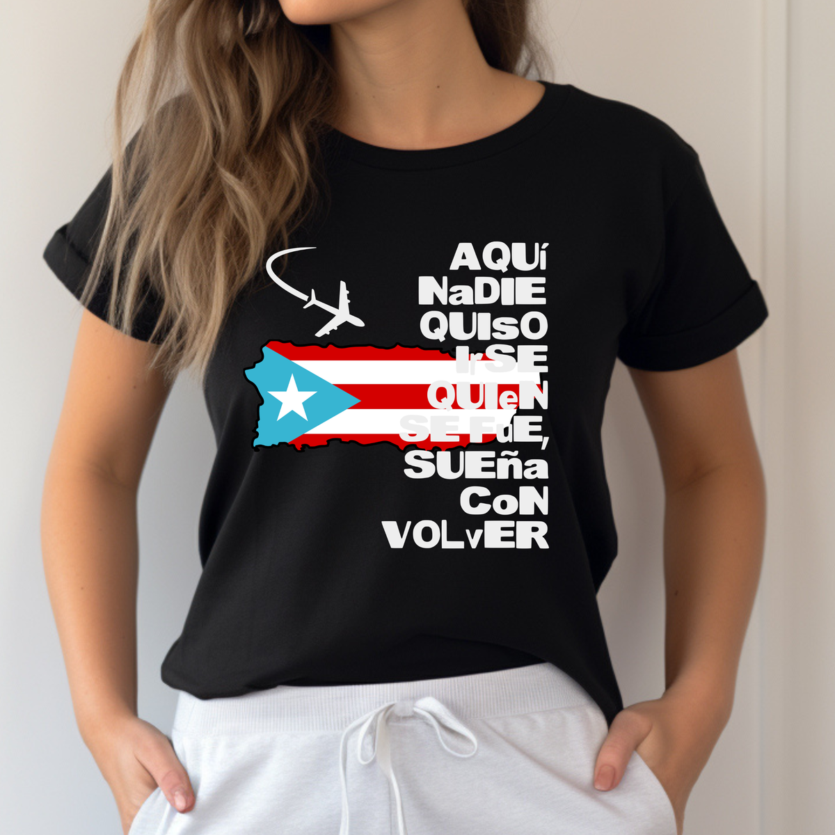 A woman wearing a black short-sleeve graphic t-shirt with a Puerto Rican flag-themed design and white sweatpants, shown from the neck down against a light neutral wall.