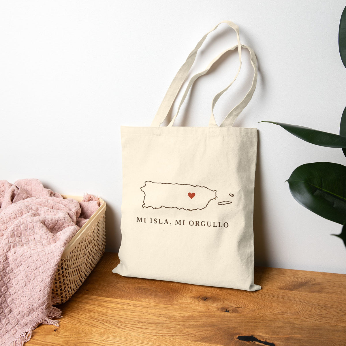 Beige tote bag with Puerto Rico' logo on a wooden surface with a white wall and plant in the background