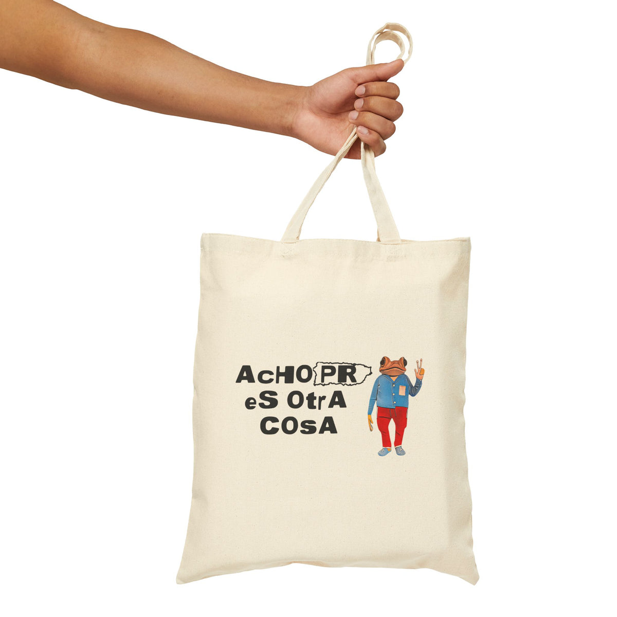 An off-white canvas tote bag with a printed graphic of a bear in a blue jacket and red pants next to the text 'AChO PR eS OtrA COSA', held by a person's arm against a plain white background.