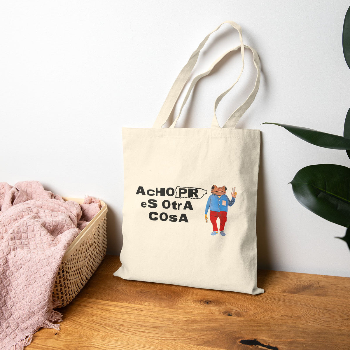 Tote bag with a scenic design of Morro Bay on a wooden surface with a plant in the background