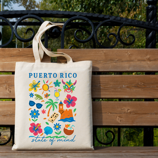 A cream canvas tote bag with 'PUERTO RICO' and colorful tropical illustrations hanging on a wooden bench outdoors. The bag features blue text and a multicolor print of flowers, palm trees, sunglasses, a beach umbrella, and a coconut.