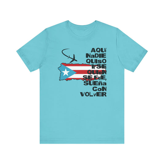 A light blue short-sleeve t-shirt with a graphic on the front featuring the Puerto Rican flag, a small airplane silhouette, and the Spanish text 'AQUí NADE QUisO QUIen SUELE, SUEÑA CoN VOLVER' in black.